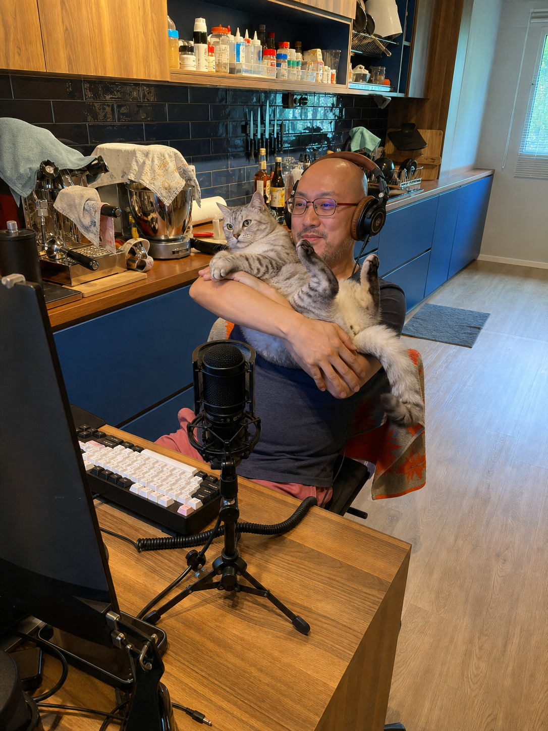 Stephen at his gaming setup, wearing headphones and holding his cat
