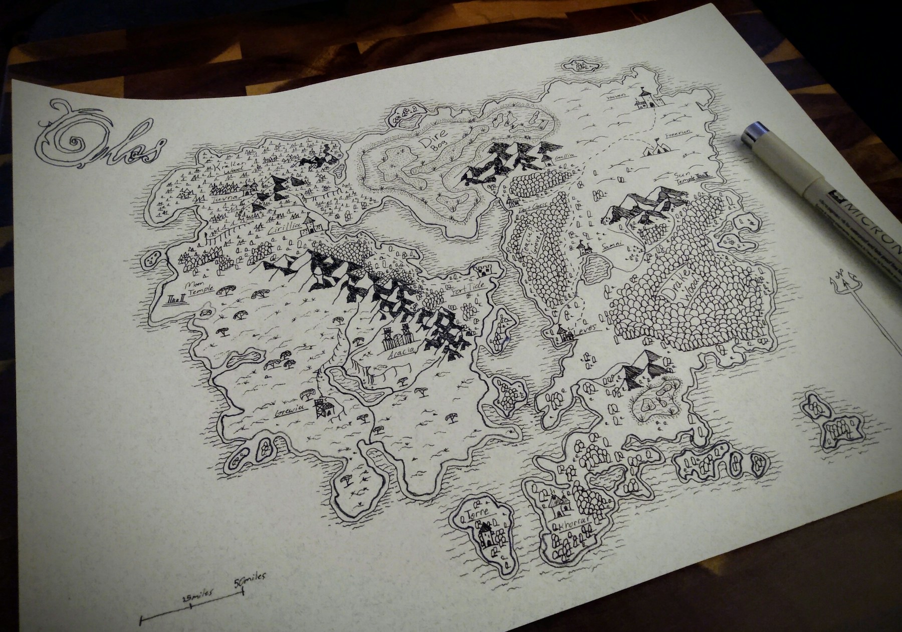 A hand-drawn fantasy map on paper with a pen beside it