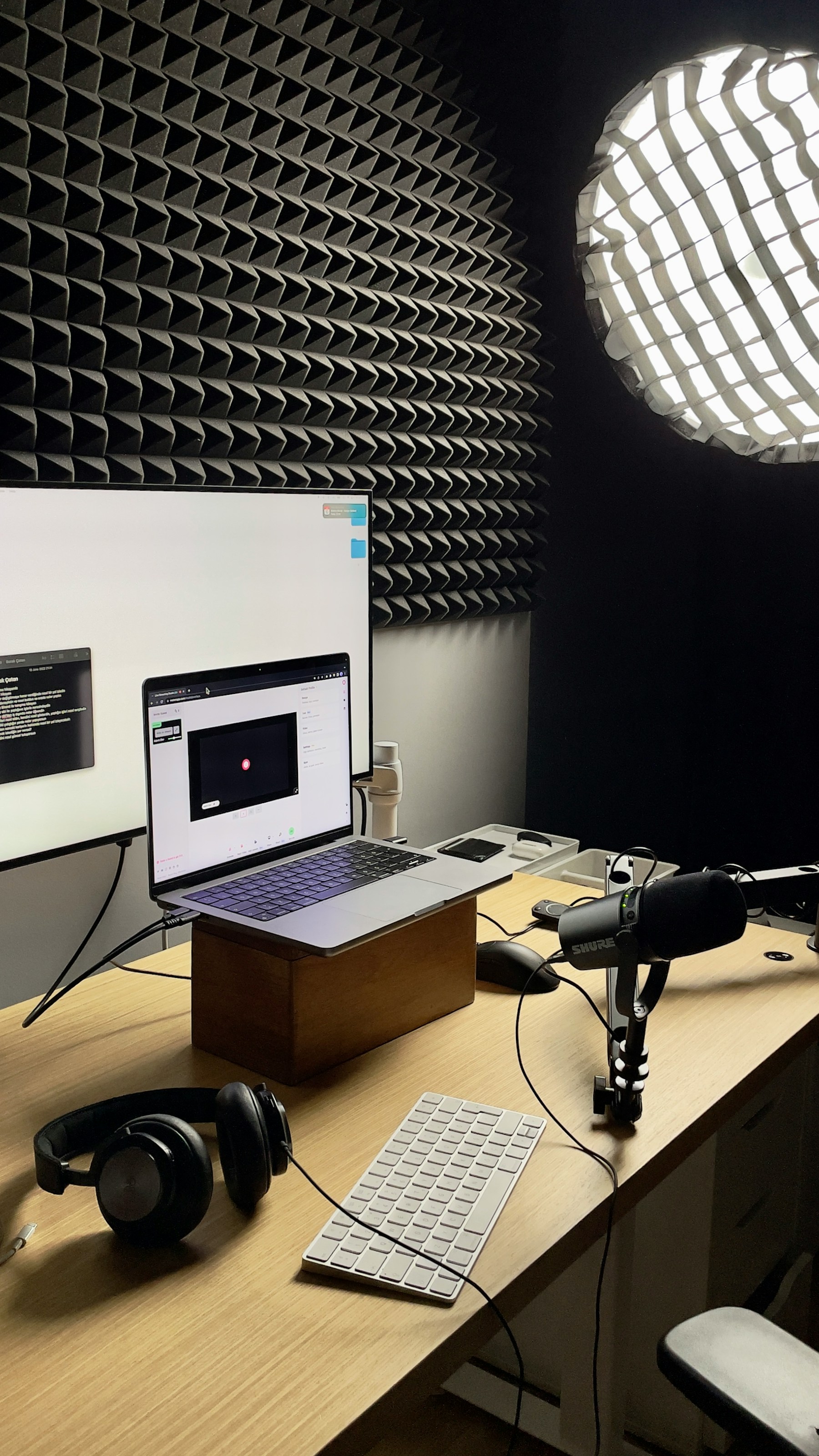 Laptop, headphones, keyboard, and screen arranged on a desk